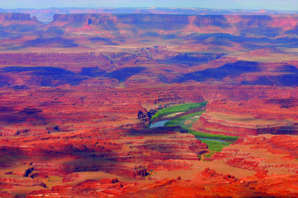 Red rock formations surround a winding green river in a vast canyon landscape. Canyonlandsbynight Canyonlands Red Rocks River