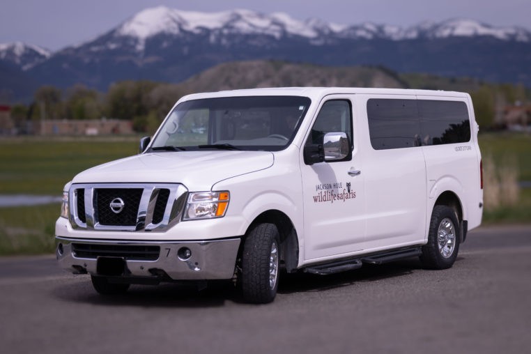 a, white, van, parked, with, mountains, nearby Jacksonholewildlifesafaris A White Van Parked With